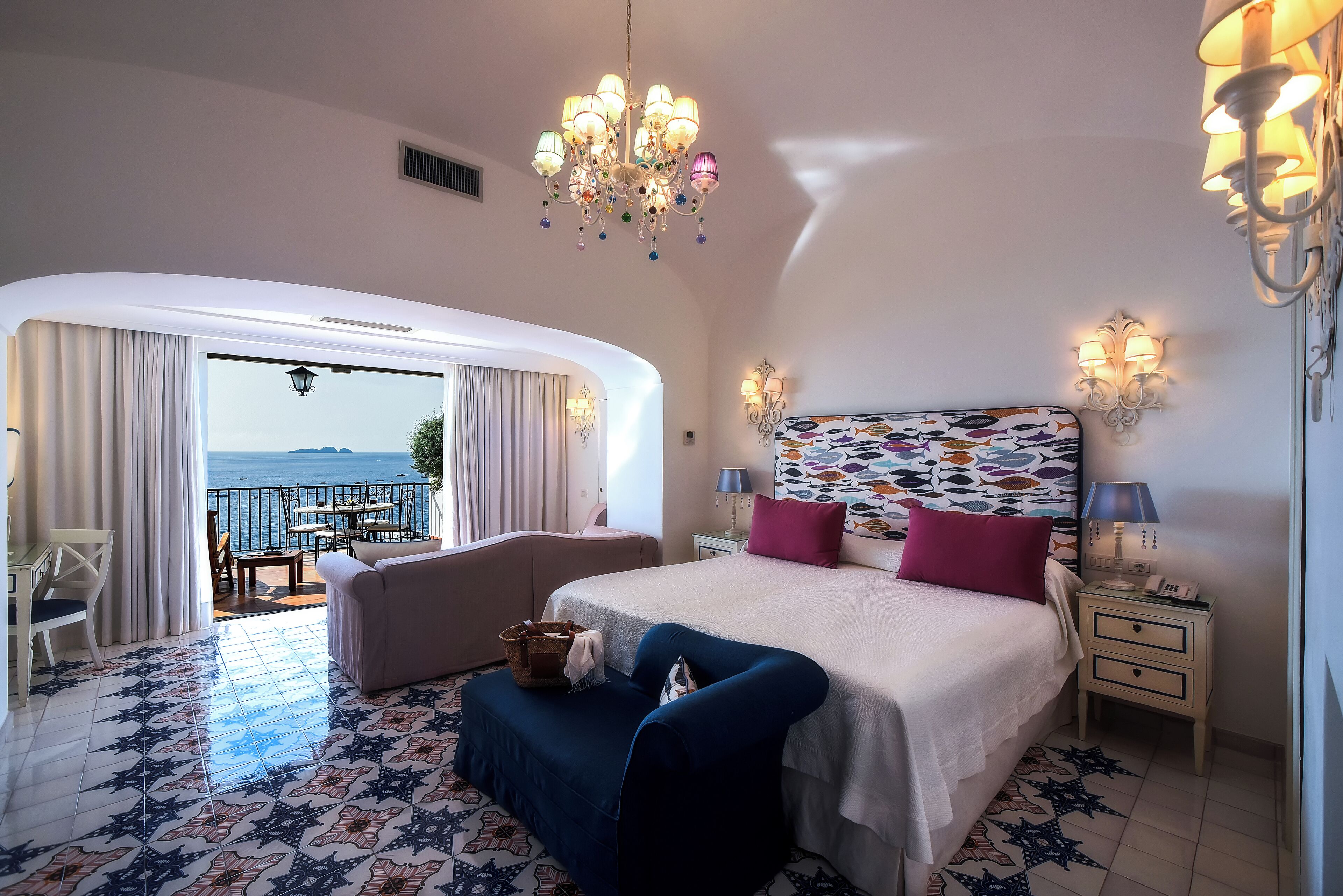 A hotel room with a large bed, a sofa, a small table, and a view of the sea.