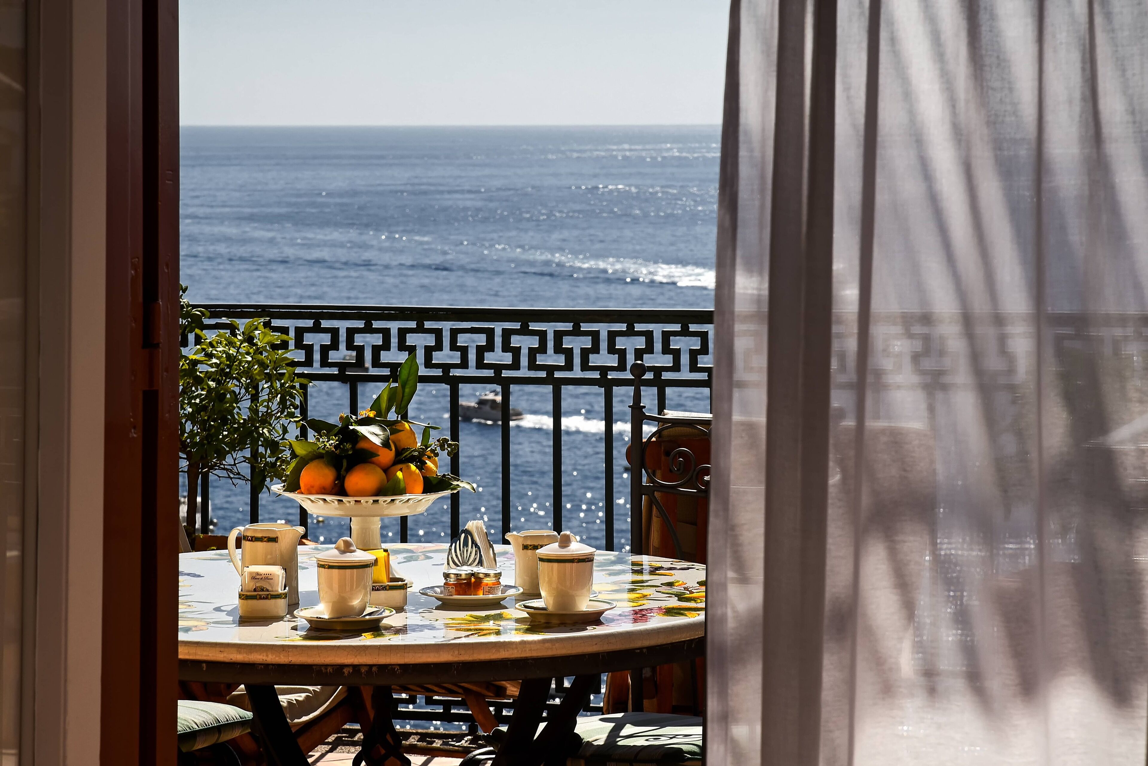 A balcony with a table set for tea, overlooking the sea.