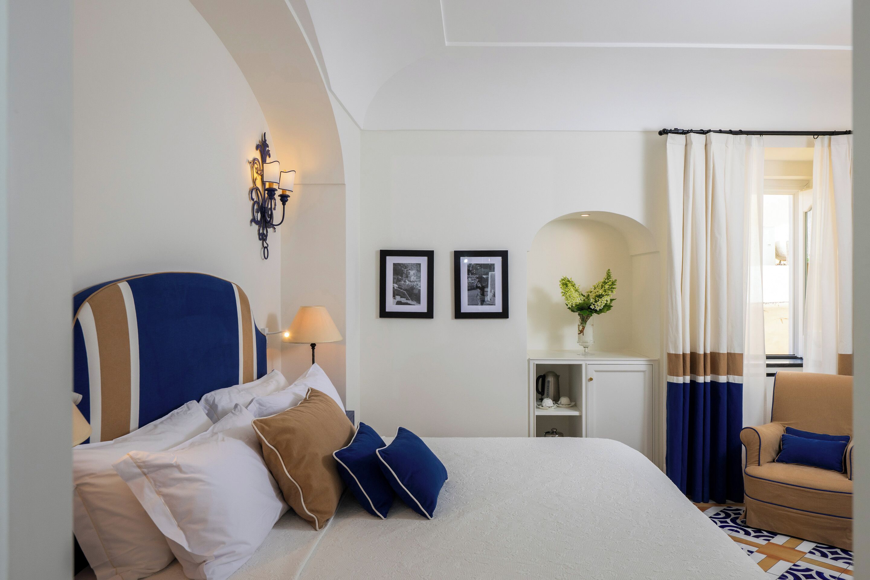 A hotel room with a bed, a chair, a lamp, a wall-mounted light fixture, and two framed pictures.