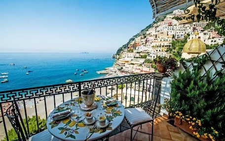 A balcony with a table set for dining, overlooking a coastal town with buildings and boats.