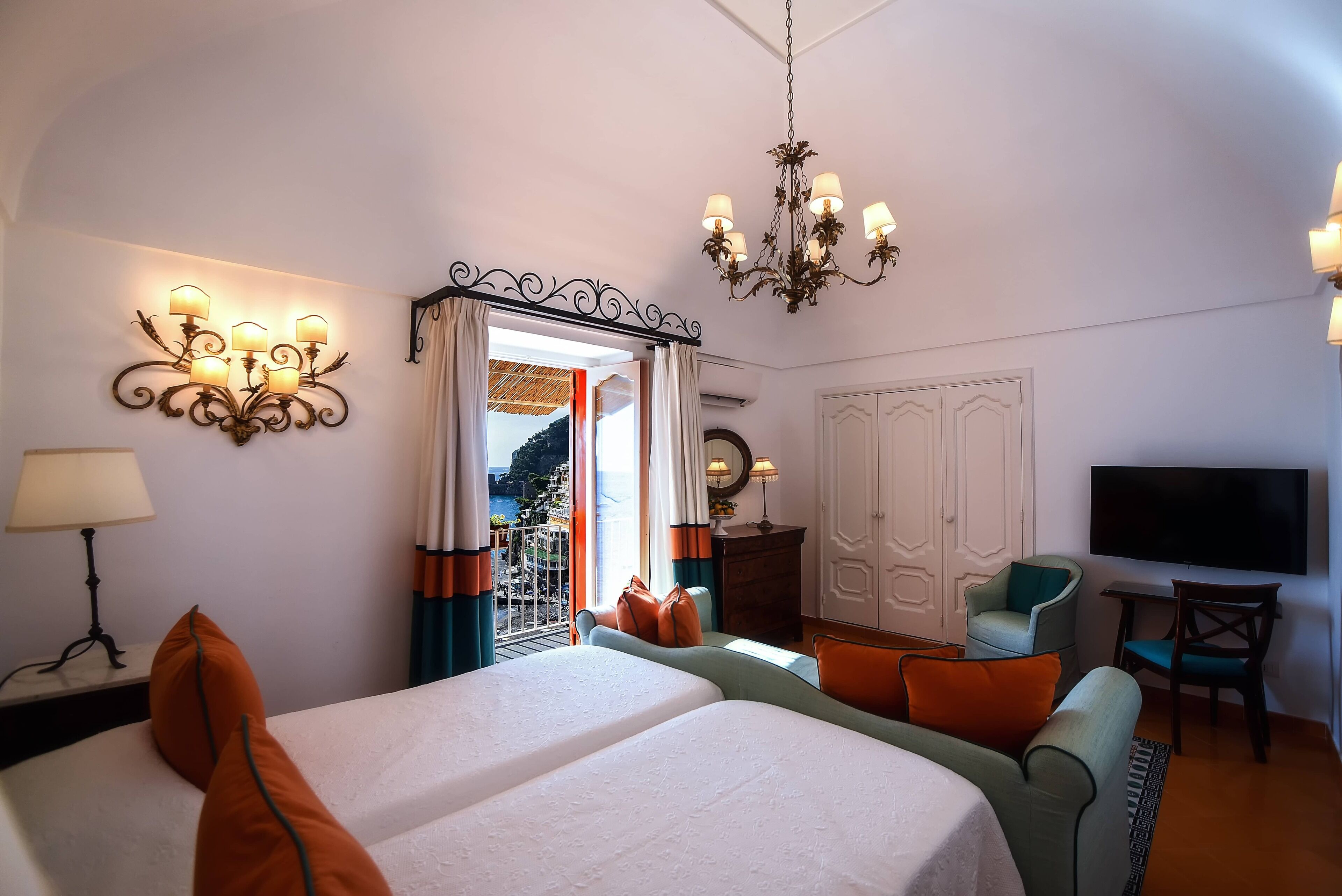 A hotel room with two beds, a sofa, a TV, and a chandelier.