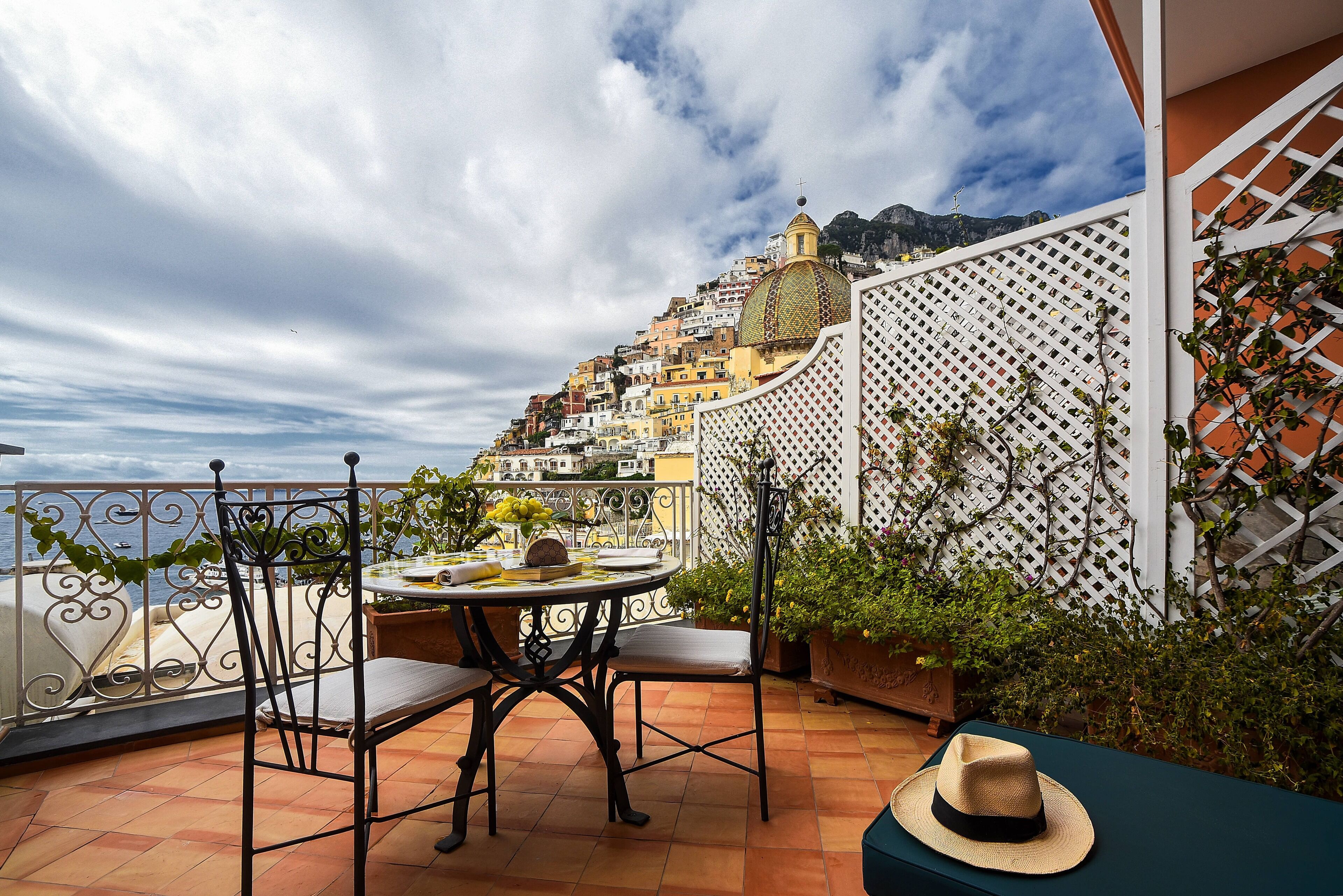 A terrace with a table and chairs, a hat on a table, and a view of a hillside town.