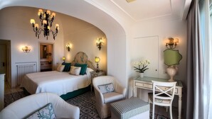 Habitación de hotel con dos camas, zona de estar con sillas, escritorio y un amplio techo abovedado.