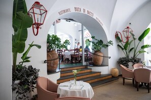 Un comedor interior con un arco blanco, plantas en macetas, muebles de mimbre y vistas al salón comedor.