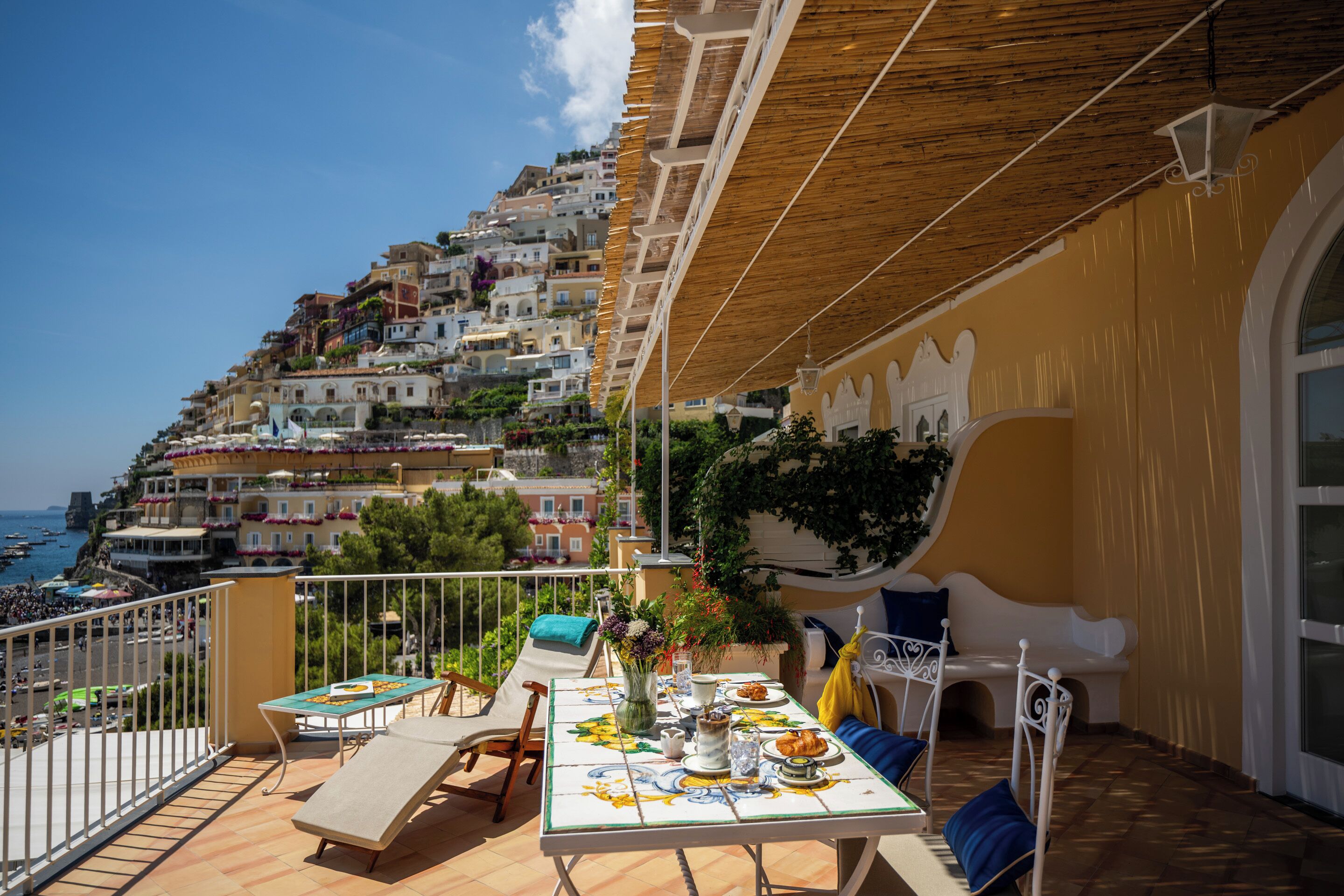 A balcony with a table set for dining, overlooking a coastal town with terraced buildings.