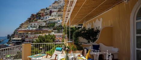 A balcony with a table set for dining, overlooking a coastal town with terraced buildings.