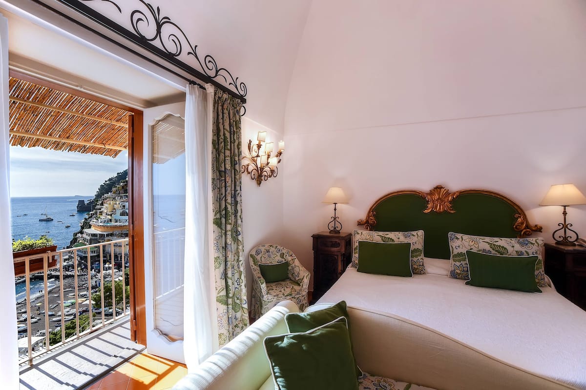 Un dormitorio con cama, almohadas verdes, una silla, una mesita de noche y vistas al mar.