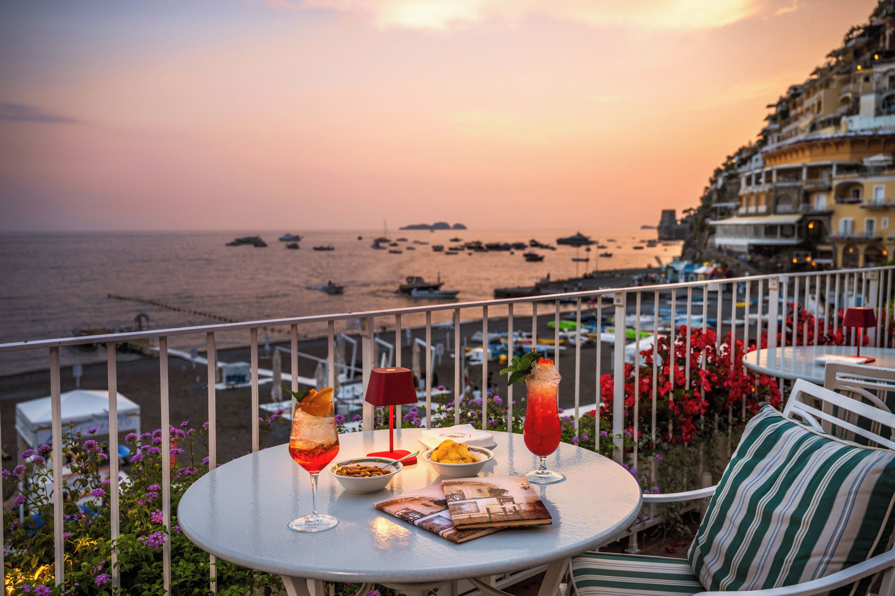 A table with drinks, snacks, and a menu on a balcony overlooking the sea.
