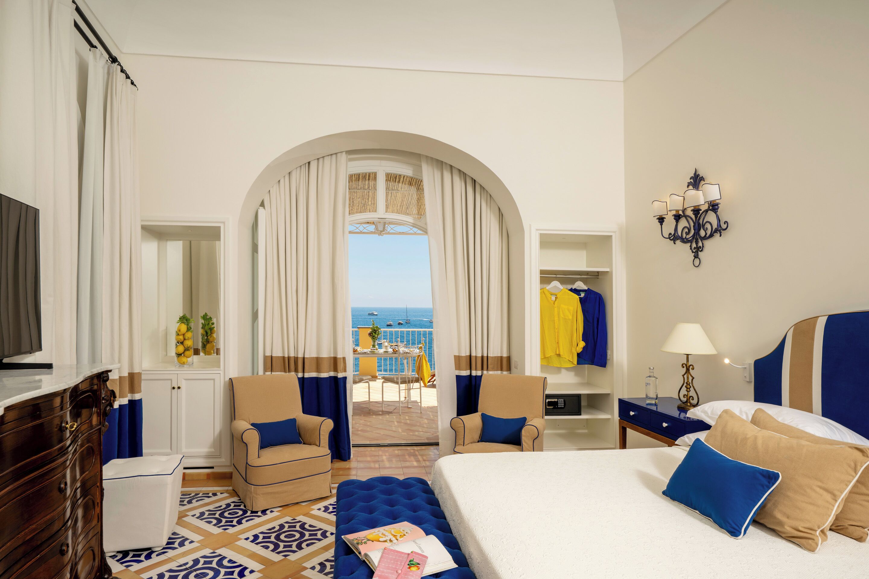 Habitación de hotel con cama, dos sillones, cómoda, tocador y vista al mar.
