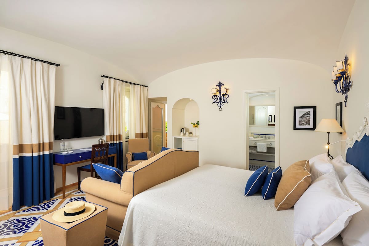 Habitación de hotel con cama, escritorio, silla, televisión y baño visible a través de un arco.