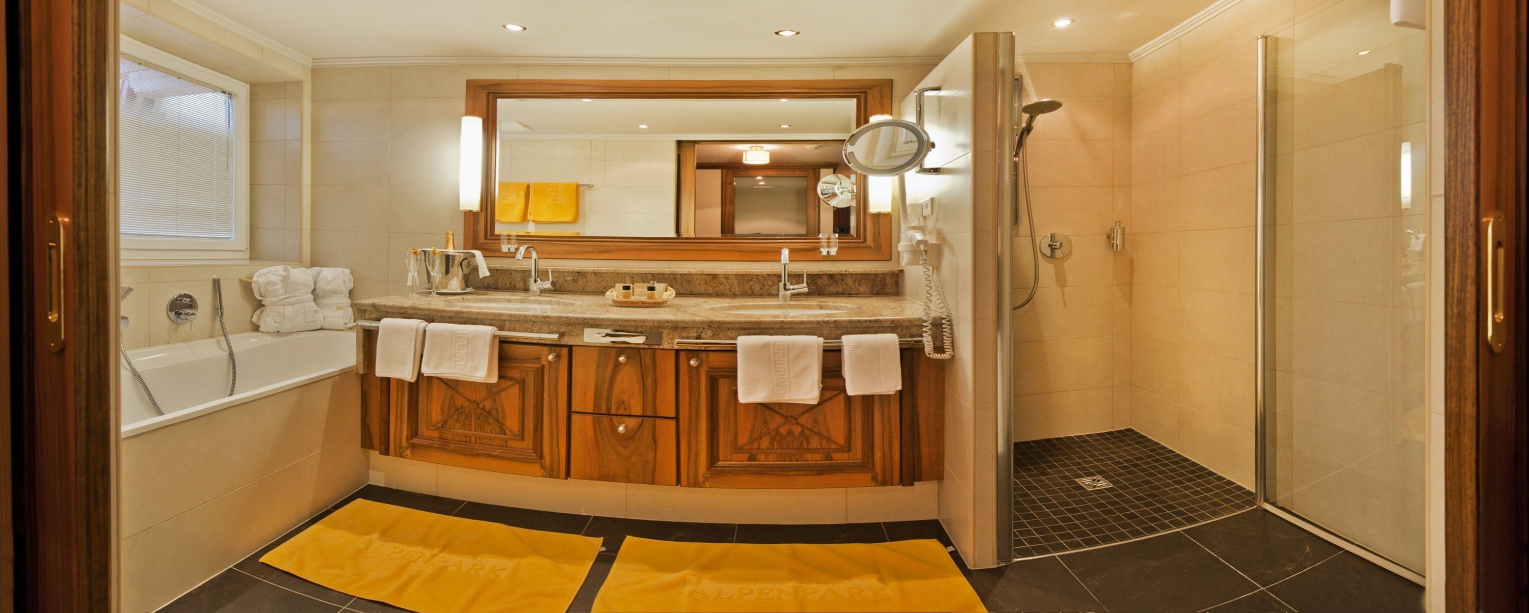 A bathroom with a bathtub, a shower, a vanity with a mirror, and a yellow rug on the floor.
