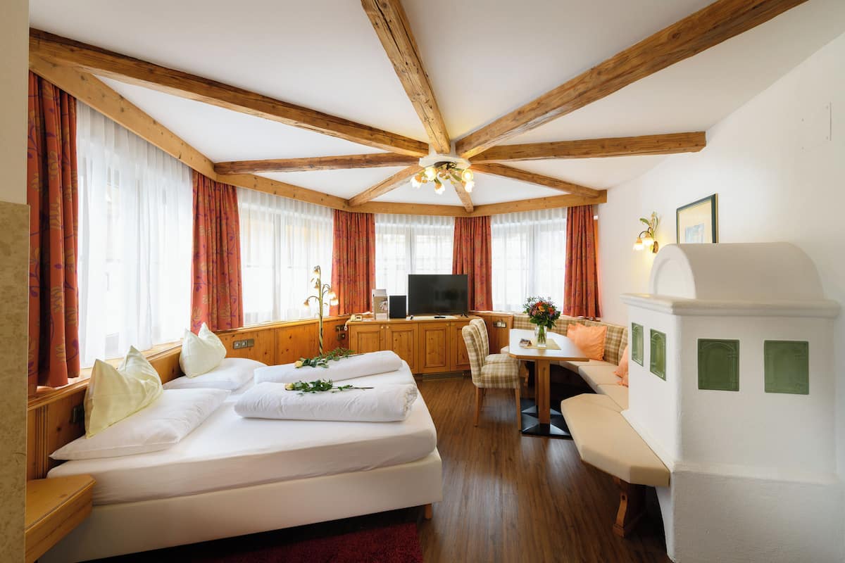A room with a wooden ceiling, a bed with white linens, a desk with a computer, a sofa, and a television.