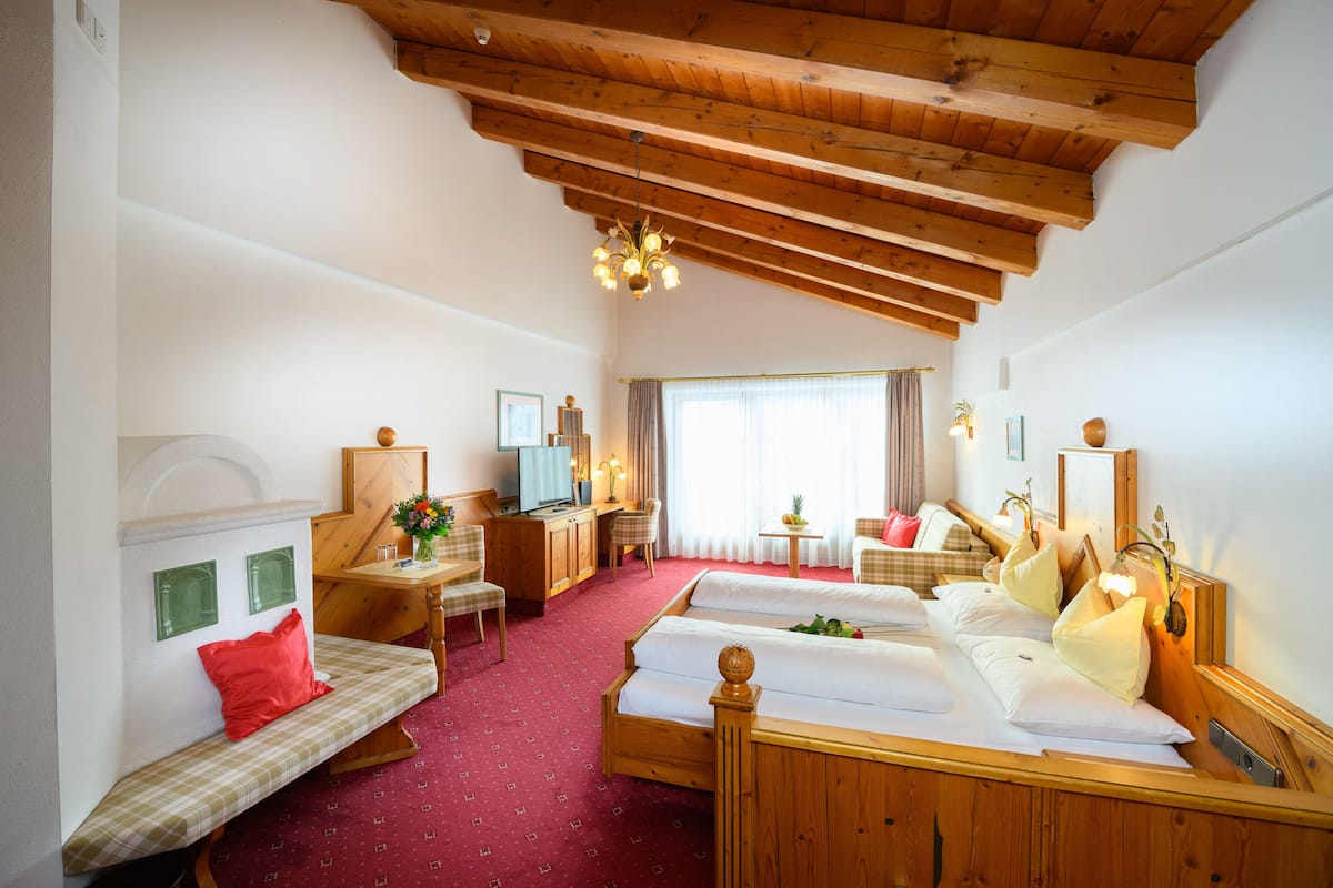 A hotel room with a wooden ceiling, two beds, a desk, a chair, and a small table with a vase.