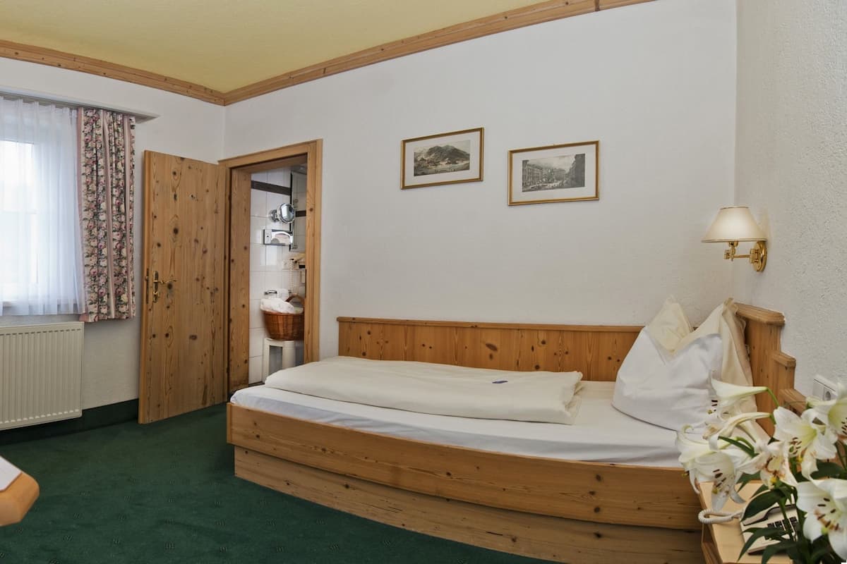 A room with a wooden bed, a table with fruit, a radiator, and two framed pictures on the wall.