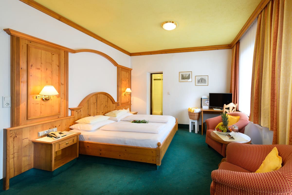 A hotel room with a wooden bed, two bedside lamps, a desk with a computer, a chair, and a small table with a fruit bowl.