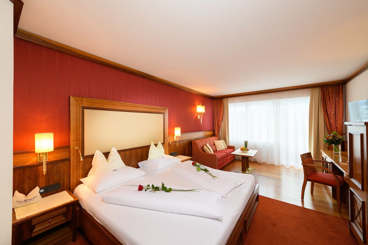 A hotel room with a large bed, a desk, a chair, a TV, and a window with curtains.