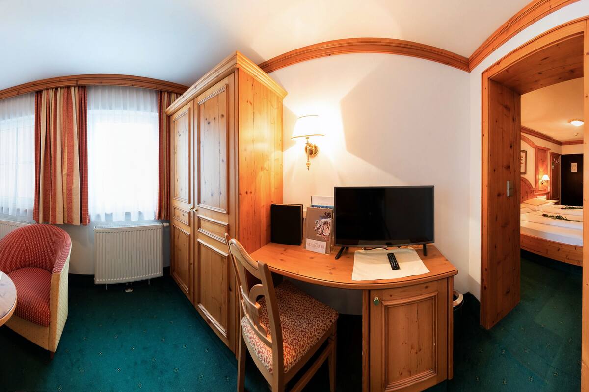 A compact hotel room with a sofa, a small table with fruit, a television, and wooden cabinets.