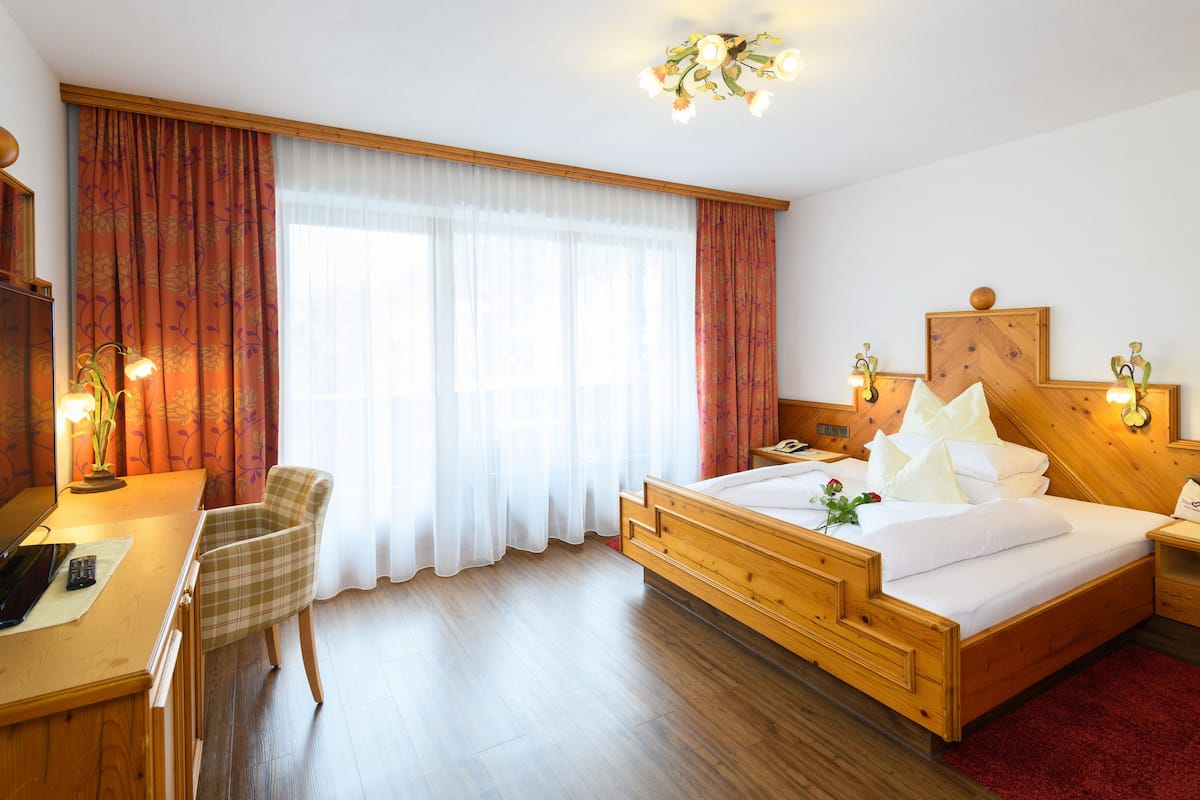A hotel room with a wooden bed, a desk with a chair, a telephone, and a nightstand with a lamp.