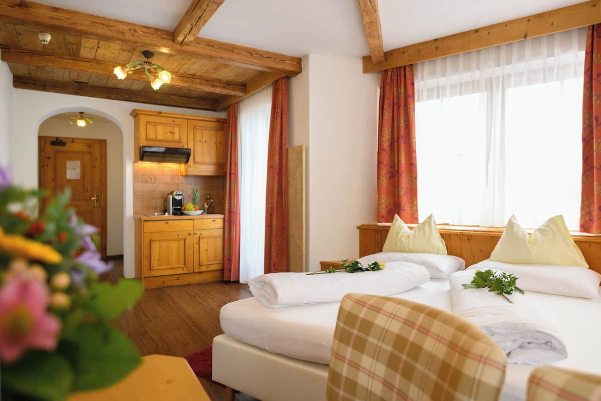 A hotel room with a bed, a wooden ceiling, a kitchen area, and a window with curtains.