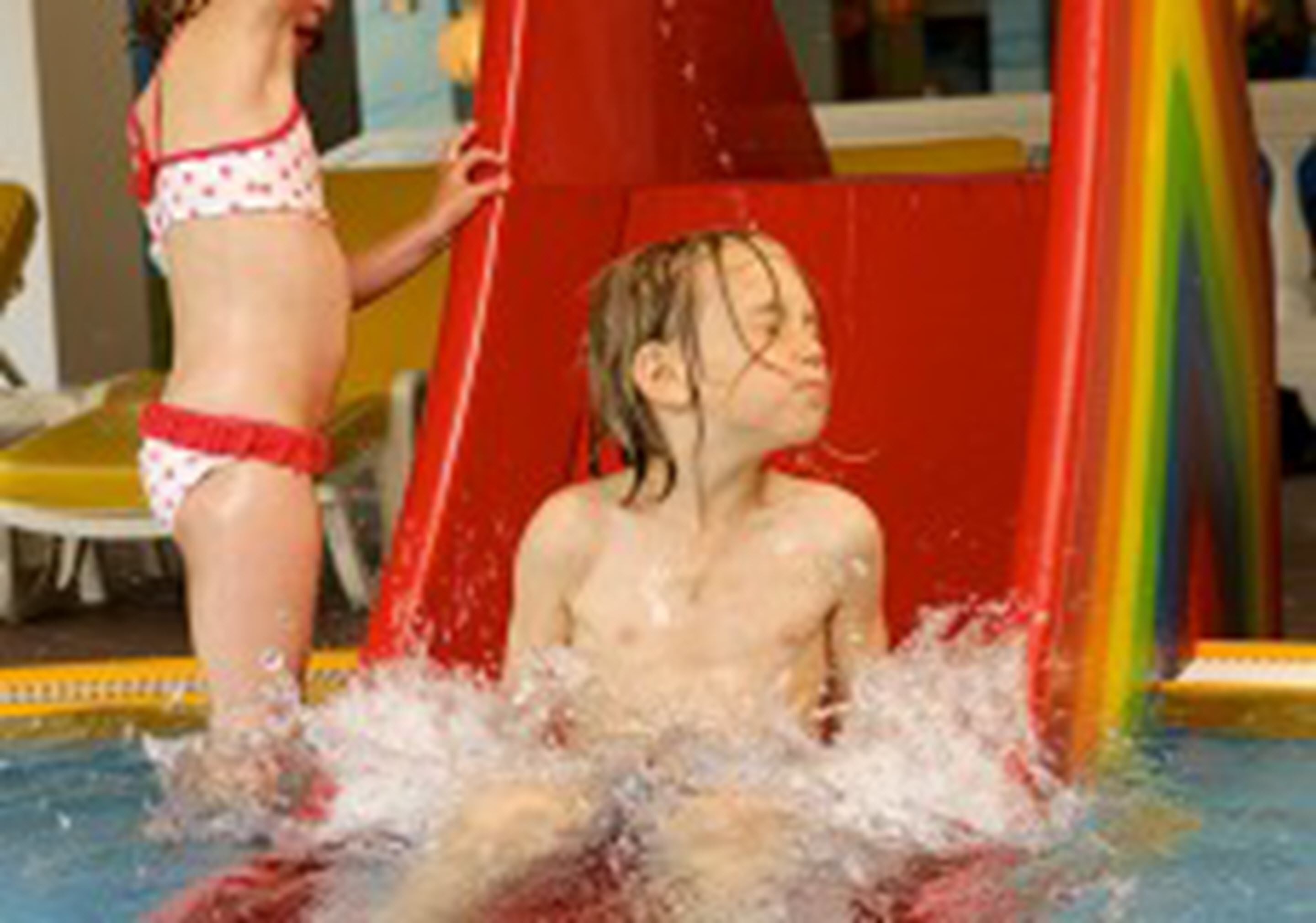 A child sliding down a water slide in a pool area.