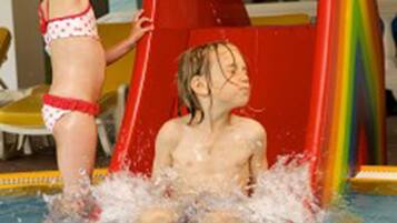 A child sliding down a water slide in a pool area.