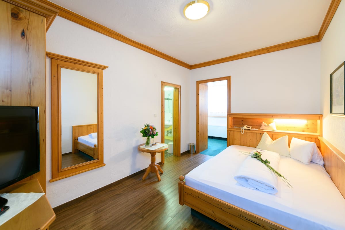 A hotel room with a wooden bed, a television, a mirror, and a small table with a vase of flowers.