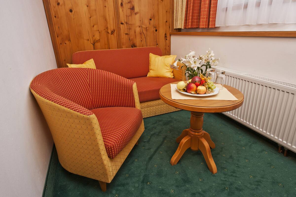 A room with a red sofa, a yellow armchair, and a small wooden table with fruit and flowers.