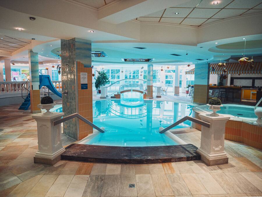 An indoor swimming pool with a glass barrier, a children's play area, and a restaurant in the background.