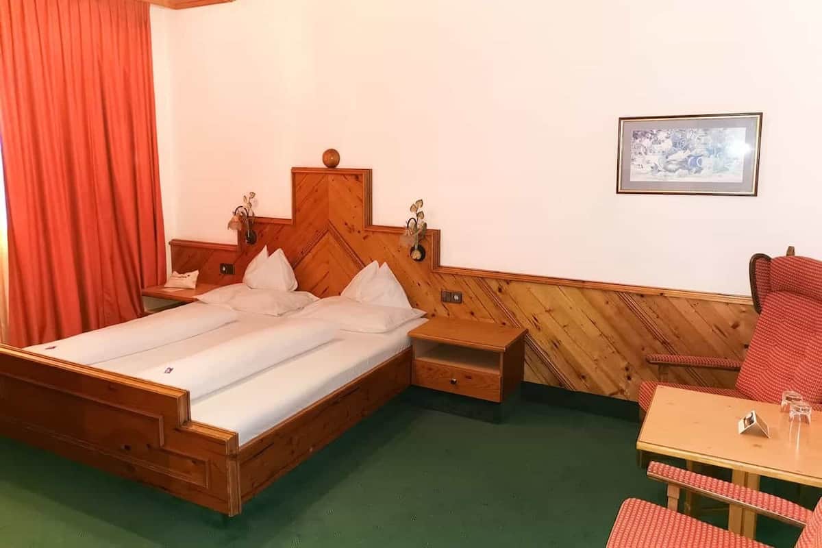 A wooden bed with a herringbone headboard, a small bedside table, a chair, and a framed picture on the wall.