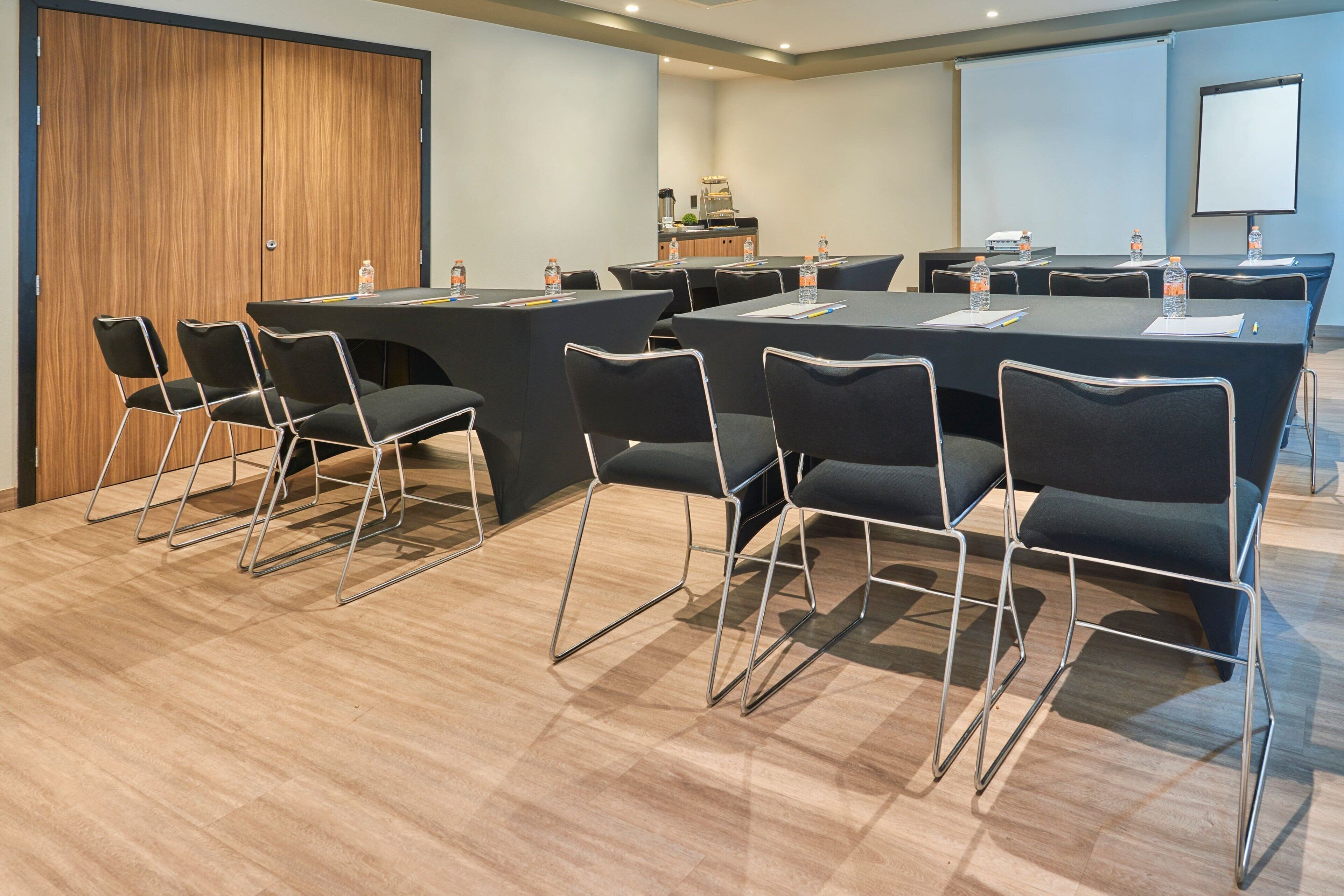 Un salón de conferencias con una gran mesa, sillas negras y una pantalla para proyector.