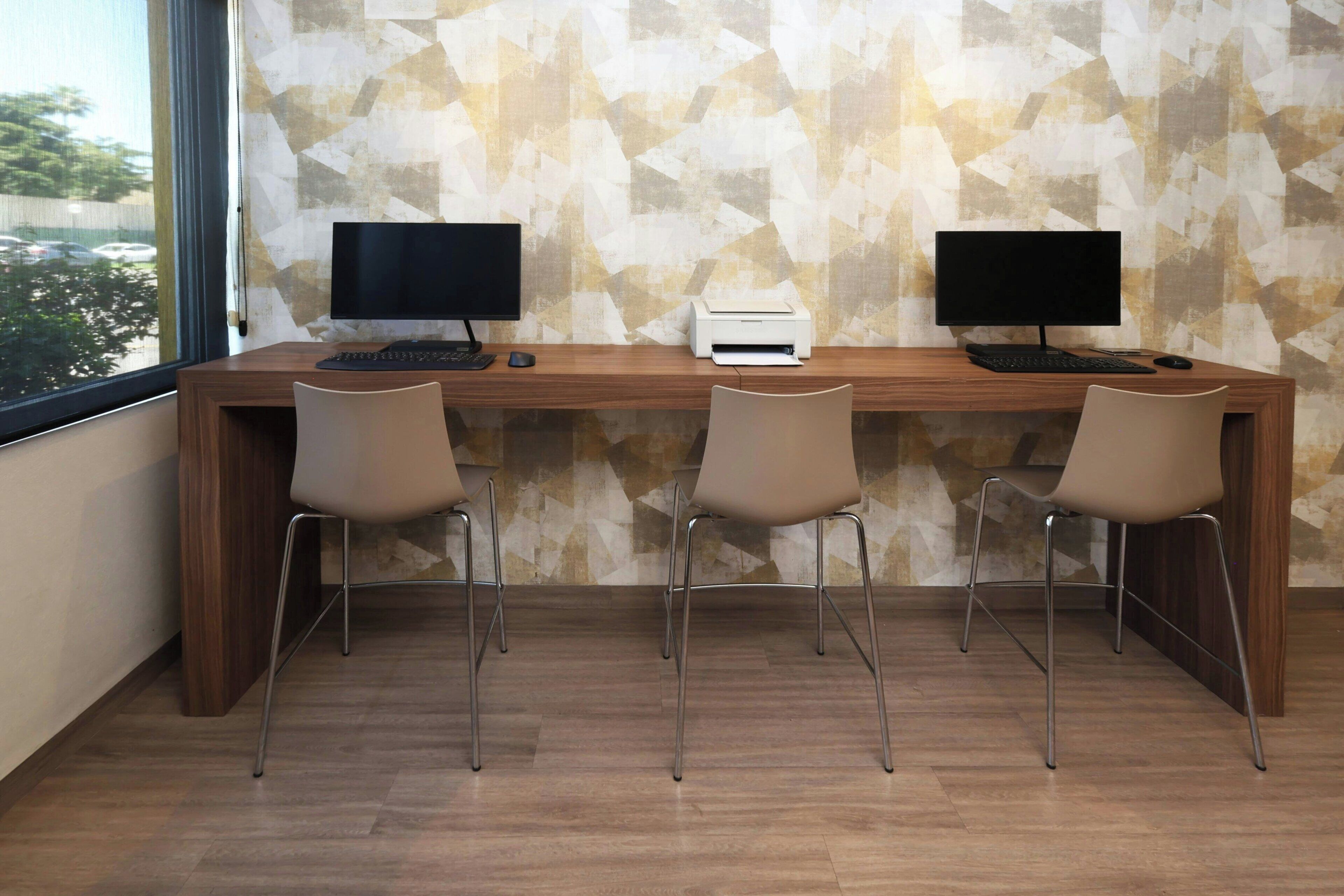 A modern office desk with two monitors, a printer, and three chairs.