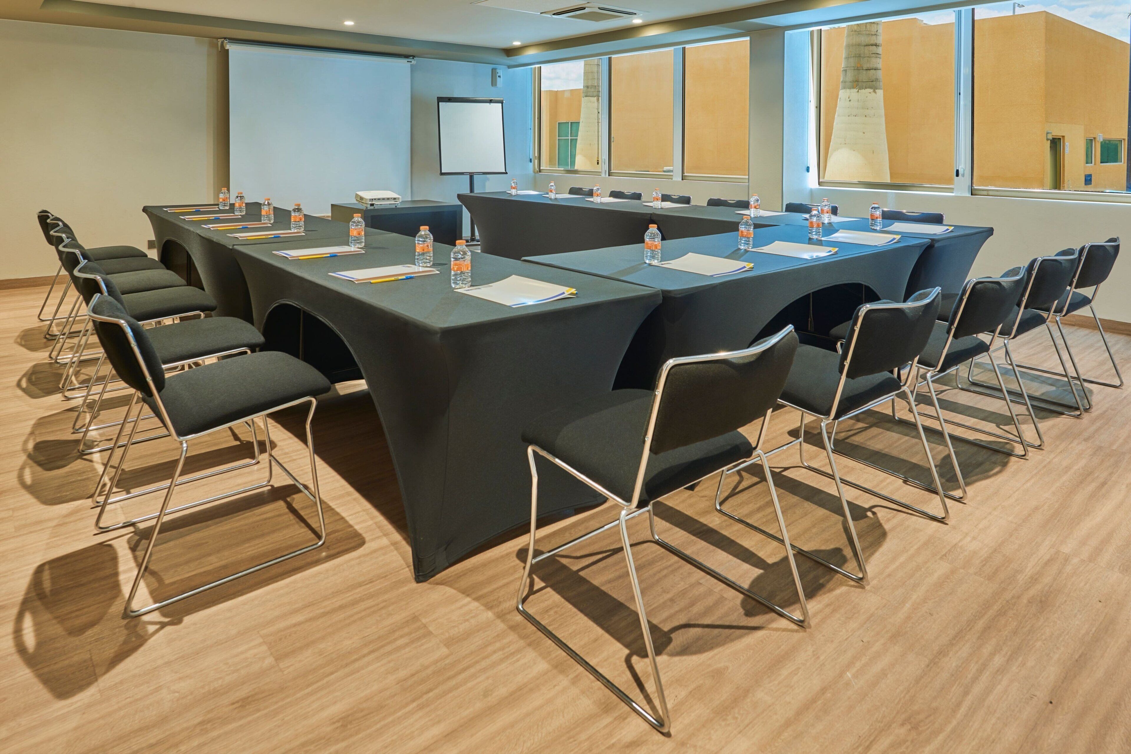 A conference room with a large table, chairs, water bottles, and a projector screen.