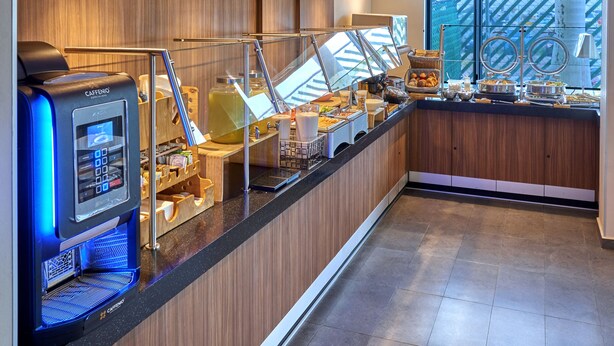 Un moderno bufé de hotel con una máquina de café, un expositor de vidrio y una variedad de alimentos.