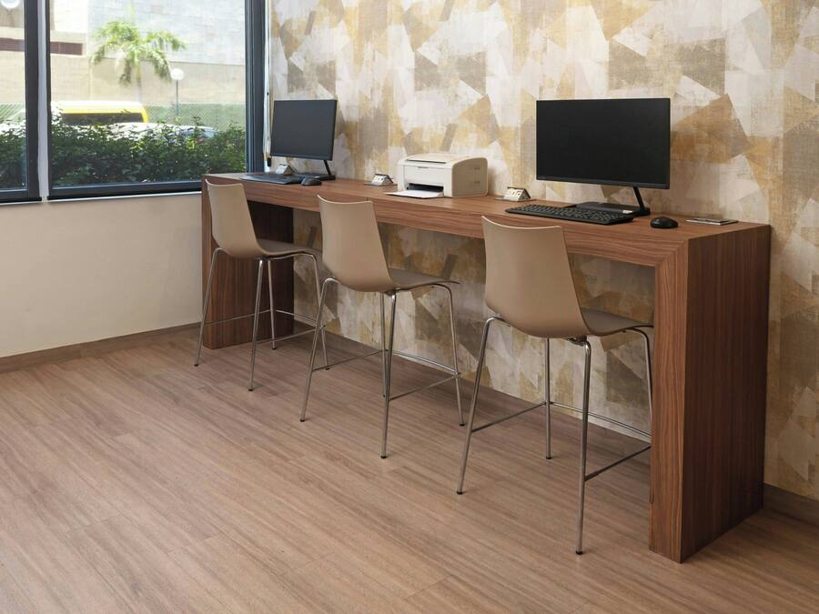 A workspace with a long wooden desk, two monitors, a printer, and three chairs.