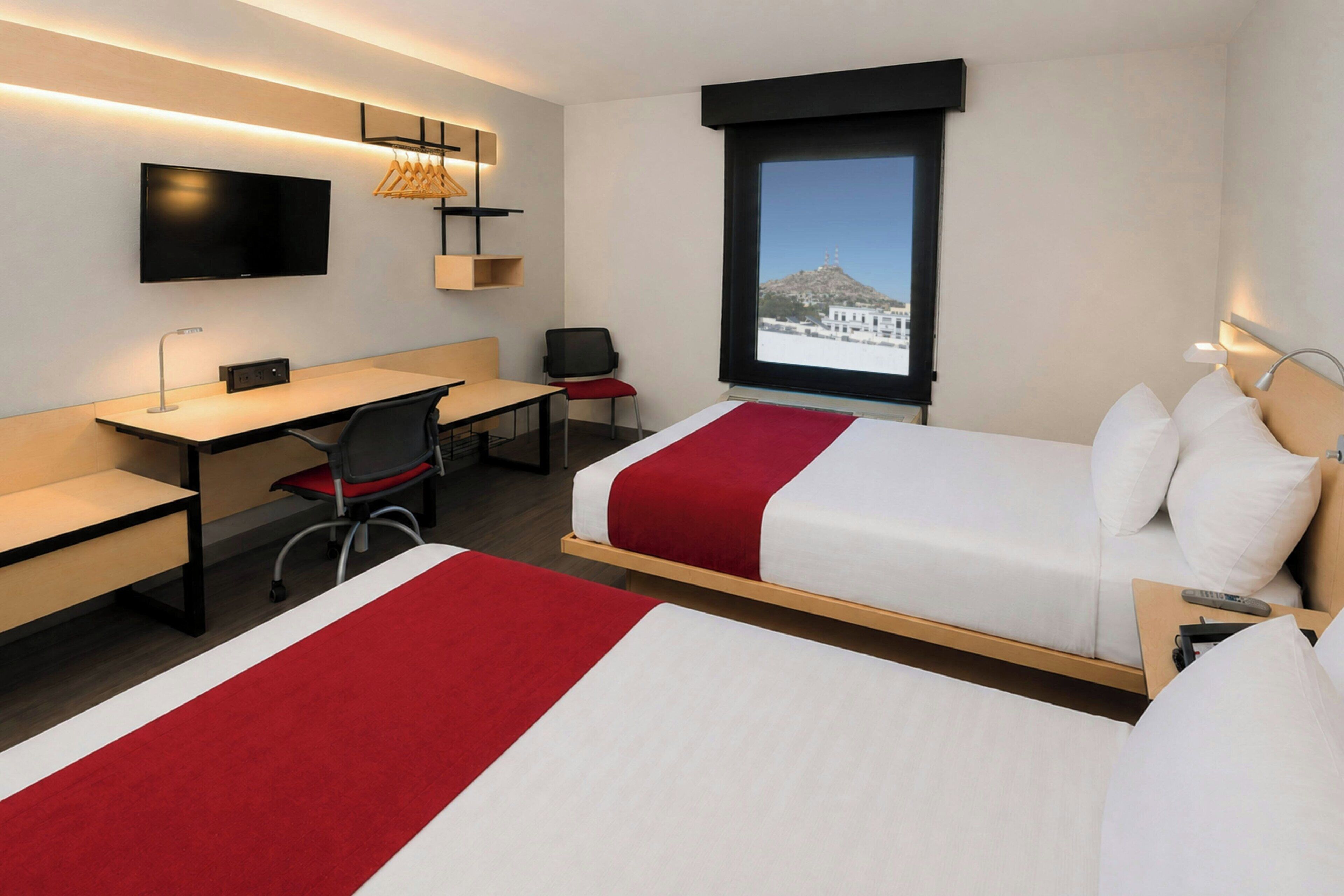 Ein Hotelzimmer mit Bett, Schreibtisch, Stuhl, Fernseher und einem Fenster mit Bergblick.