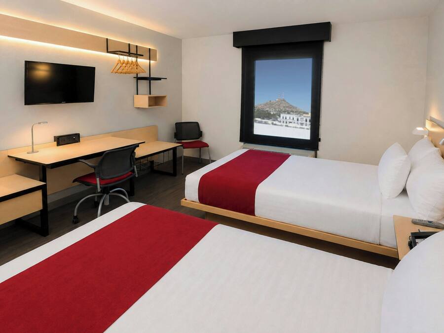 A hotel room with a bed, desk, chair, TV, and a window with a mountain view.