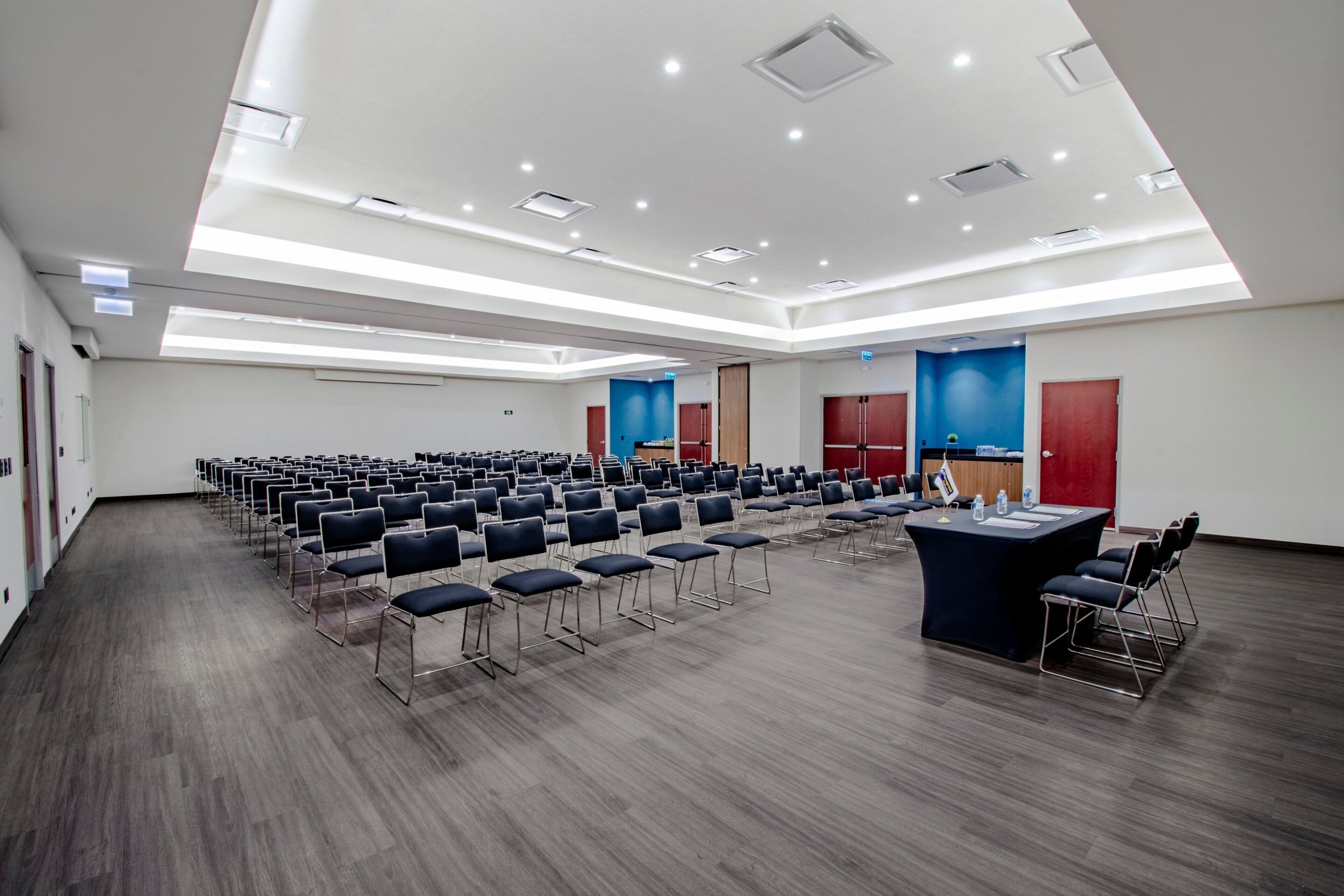 Un salón de conferencias con filas de sillas, un atril y una gran mesa.