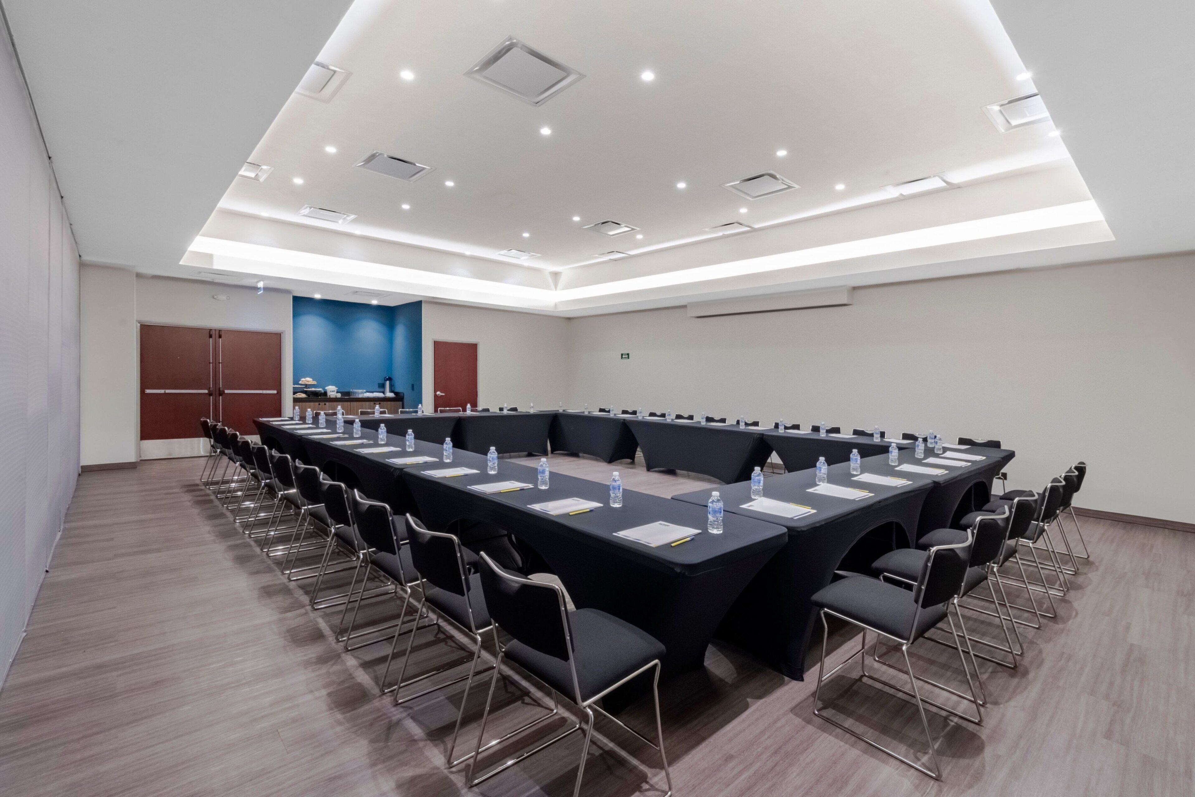 Une salle de conférence avec une longue table, des chaises et des bouteilles d’eau.