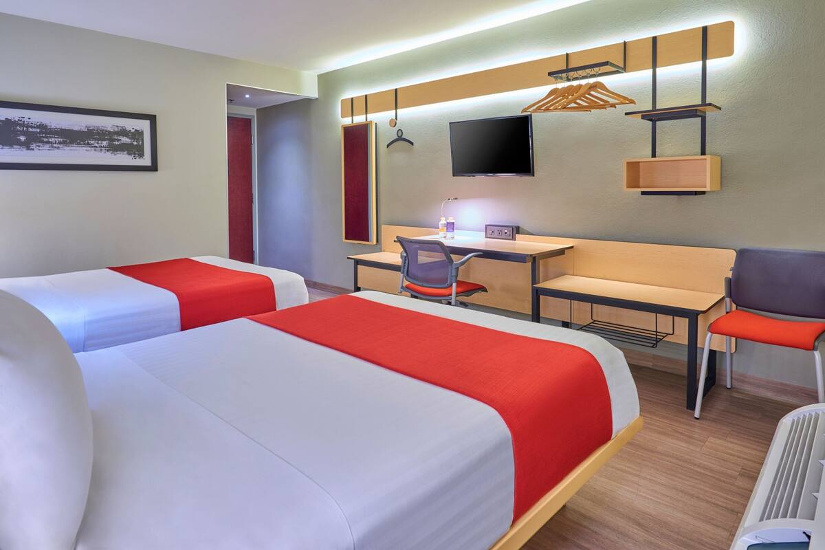 A hotel room with two beds, a desk with a chair, a TV, and a coat rack.