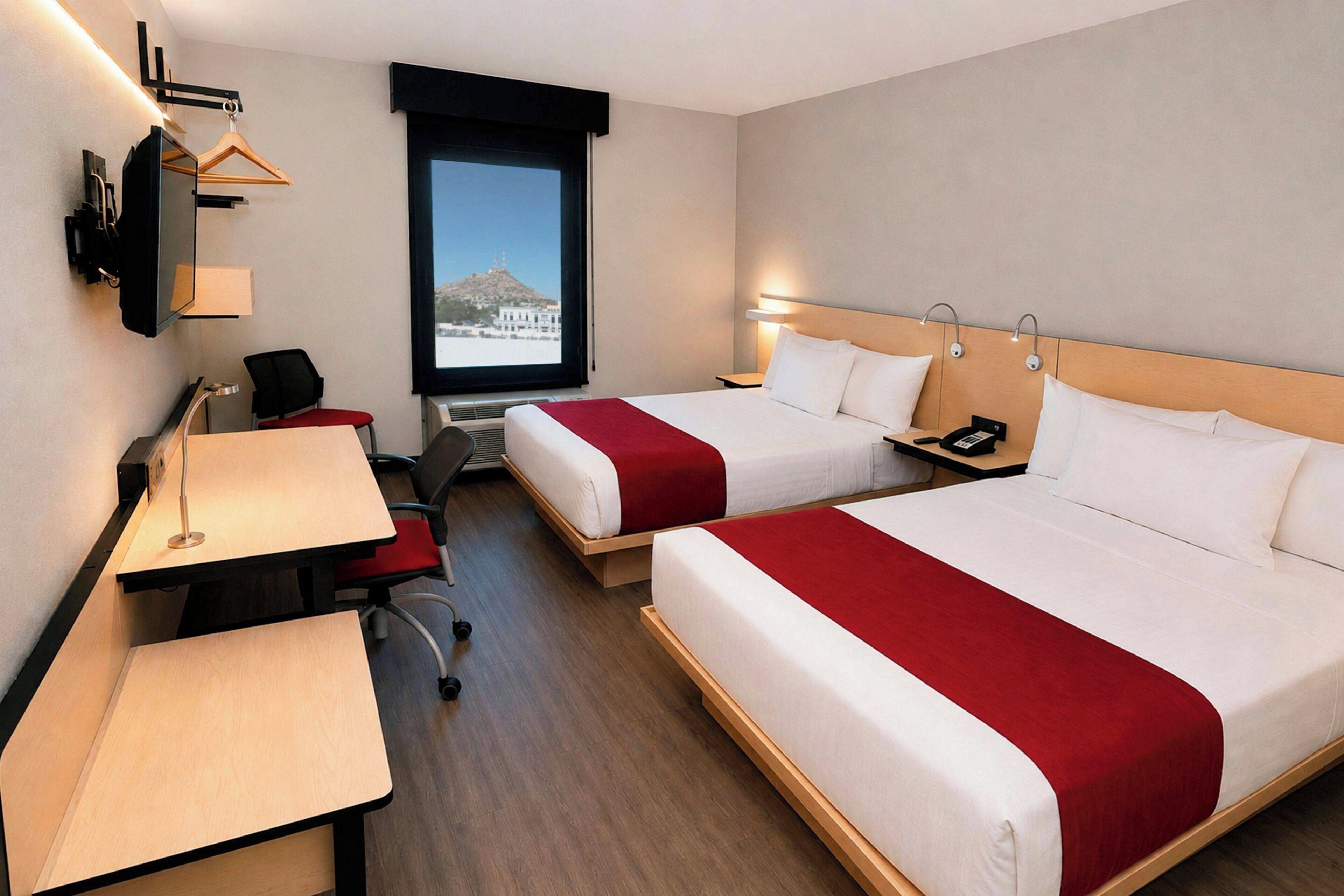 Een hotelkamer met twee bedden, een bureau, een stoel, een televisie en een raam met uitzicht.