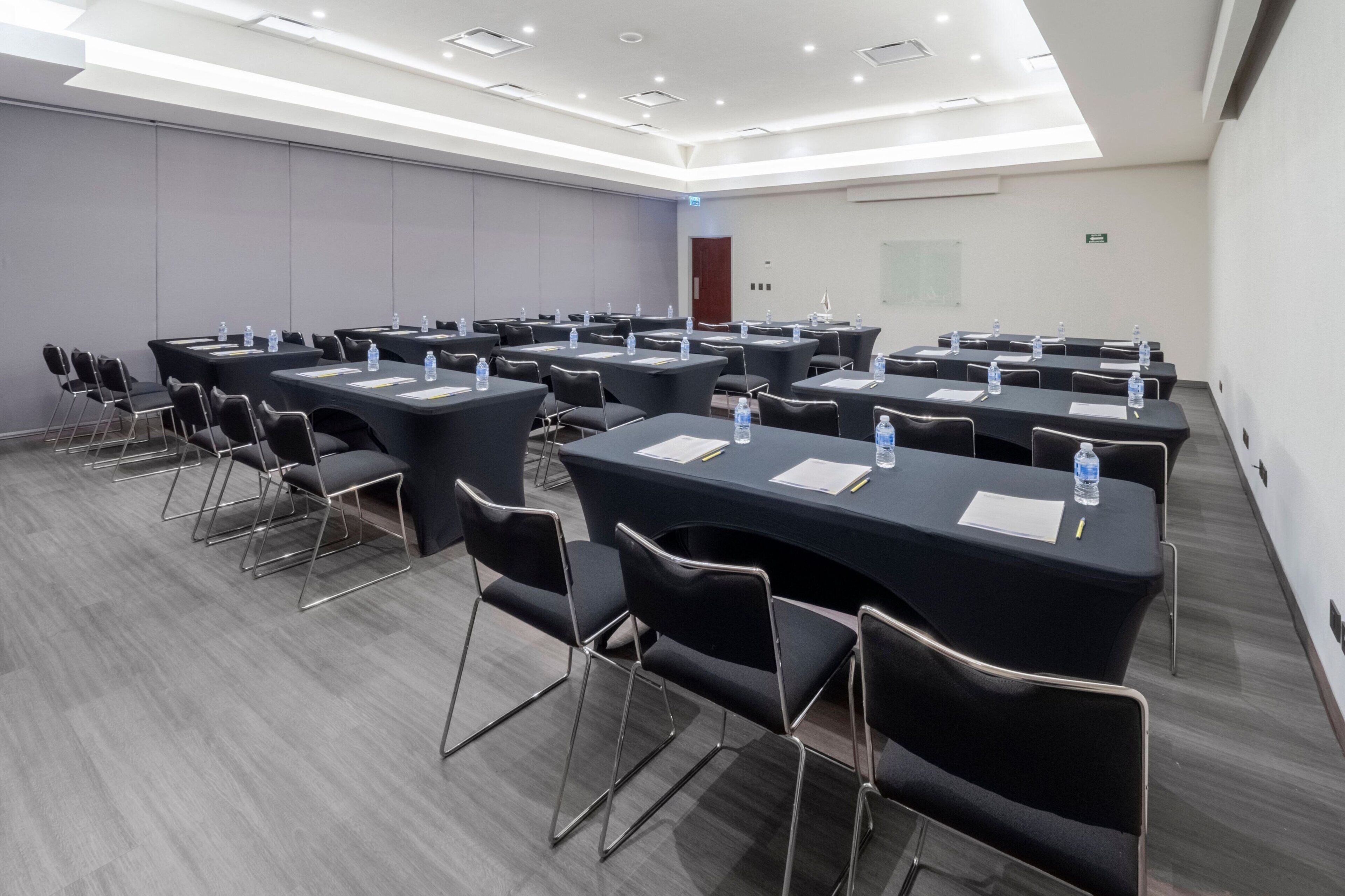 Une salle de conférence dotée de plusieurs tables et chaises, ainsi que de bouteilles d’eau et de documents.