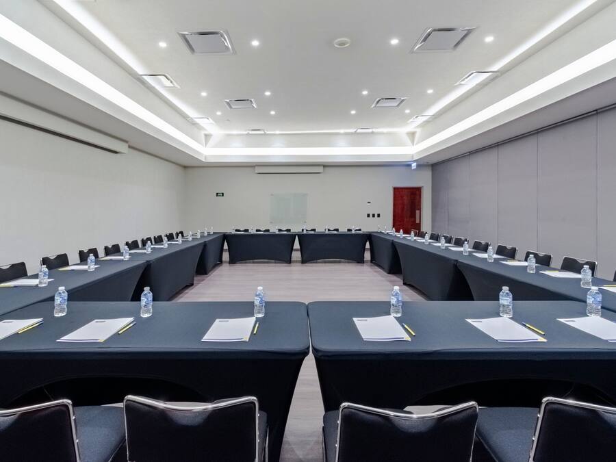 Un salón de conferencias con una larga mesa, sillas, botellas de agua y documentos.