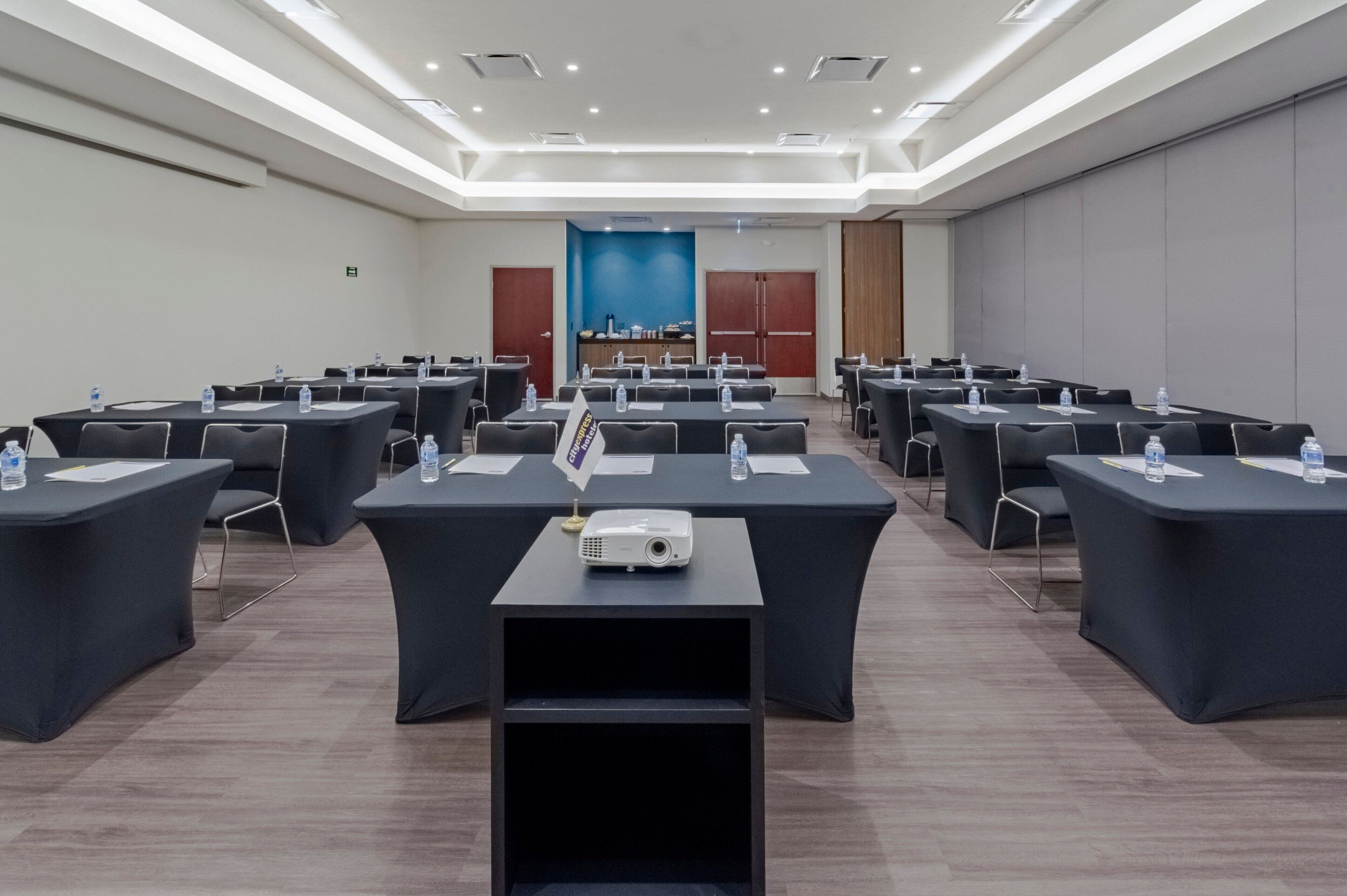A conference room with multiple tables, each equipped with a projector, water bottle, and name tag.