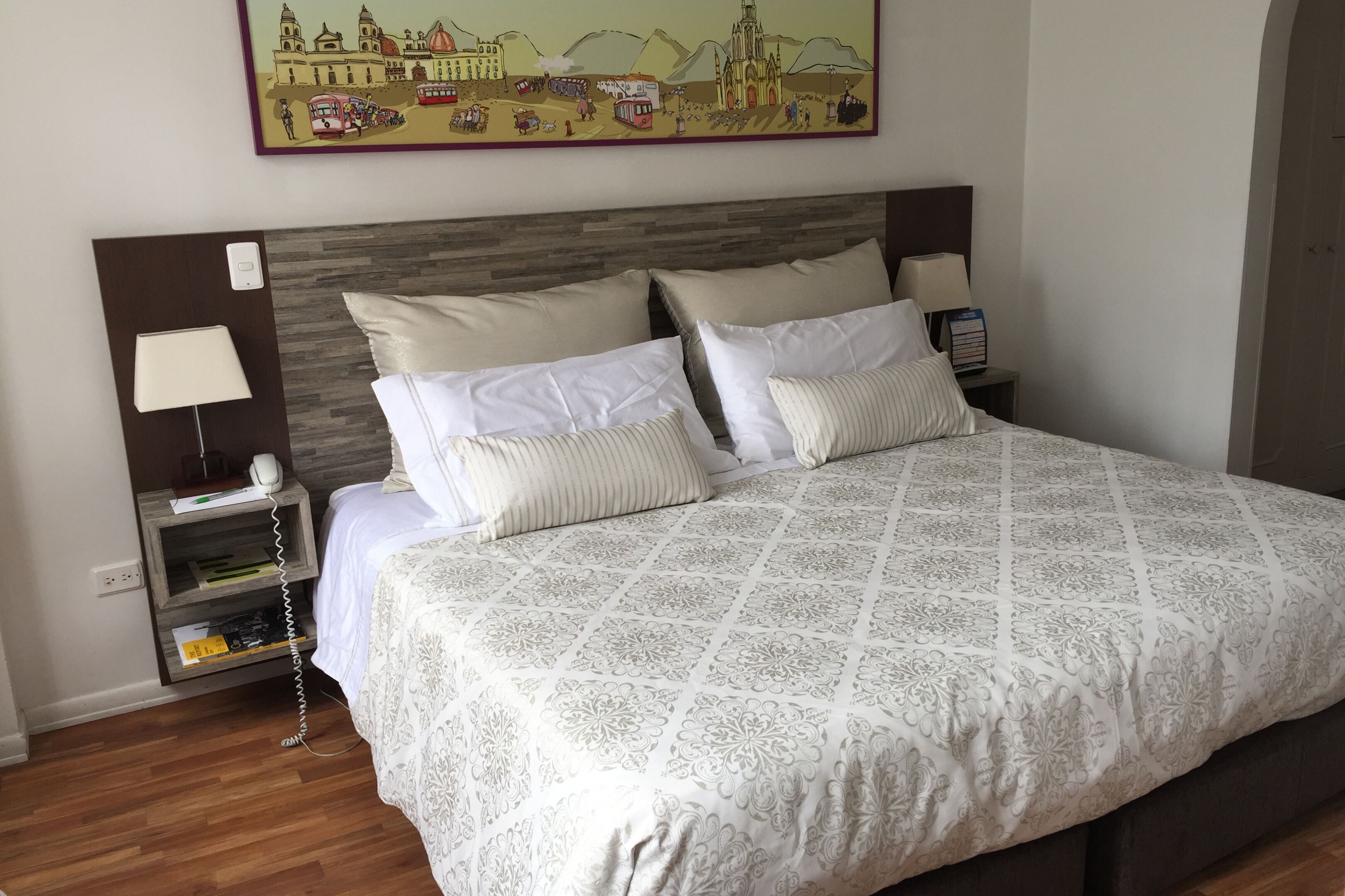 A neatly made bed with a patterned bedspread, a bedside lamp, and a nightstand with a lamp and a phone.
