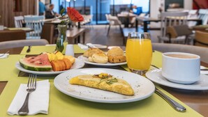 Uma mesa de café da manhã com omelete, frutas, croissants, suco de laranja e café, sobre um jogo americano verde.