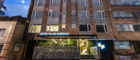 A multi-story hotel with a brick facade, large windows, and a sign reading "HOTEL VILAR AMERICA".