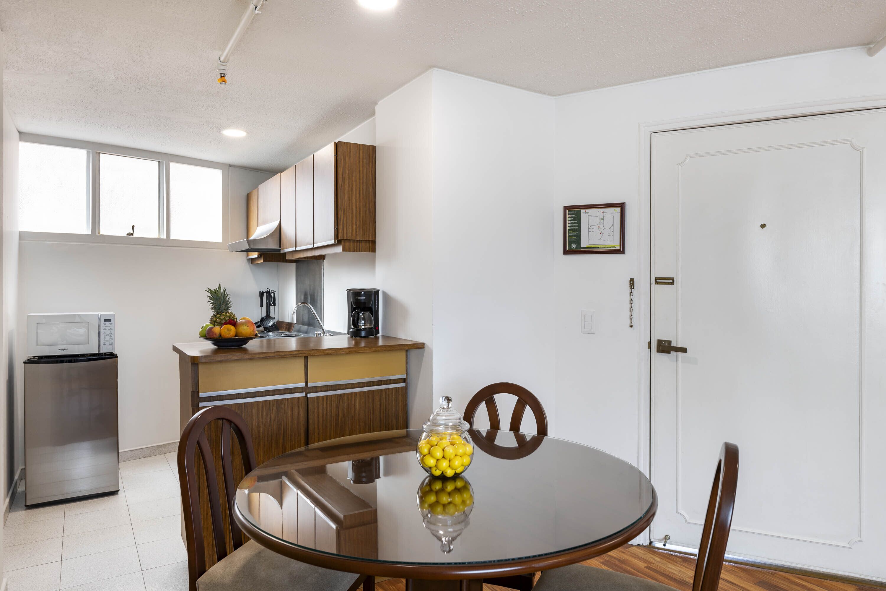 A compact kitchen with a microwave, refrigerator, wooden cabinets, and a dining table with chairs.