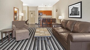 A modern living room with a sofa, armchair, and coffee table, a kitchen in the background, and a framed picture on the wall. - Best Western Plus Meridian Hotel (Lloydminster)