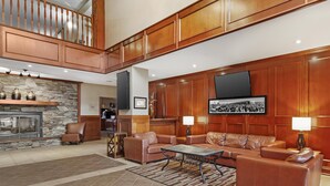 A spacious lobby with a stone fireplace, leather sofas, a flat-screen TV, and wooden paneling. - Best Western Plus Meridian Hotel (Lloydminster)