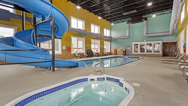 An indoor swimming pool with a blue slide, multiple lounge chairs, and a clear view of the pool area. - Best Western Plus Meridian Hotel (Lloydminster)